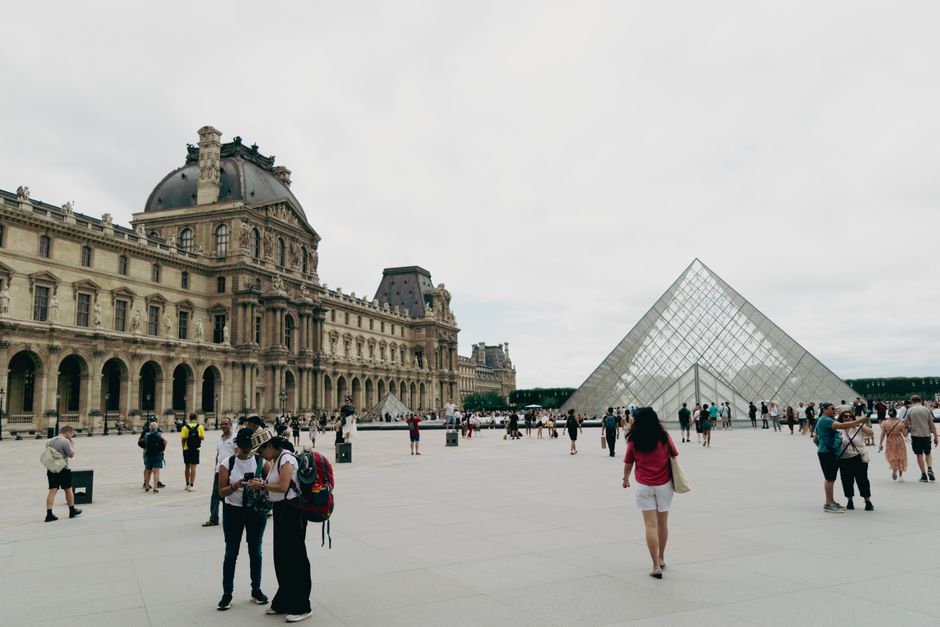 Crowds gather around the iconic Louvre and Pyramid in Paris, showcasing French architecture and culture.
