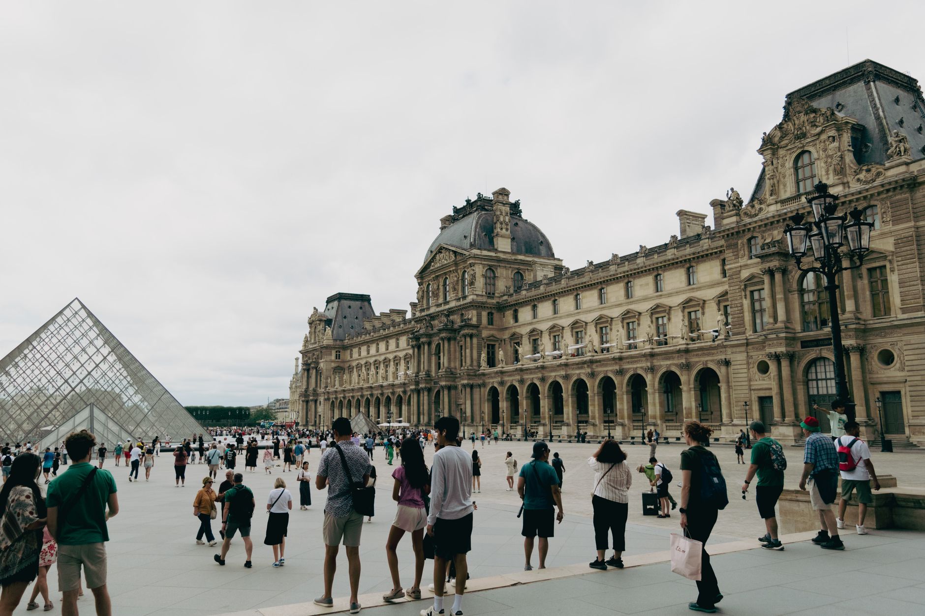 Visitors gather at the Louvre Museum in Paris with the iconic glass pyramid in view.