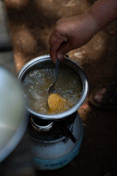 Close-up of a hand stirring soup in a pot over a portable outdoor stove.