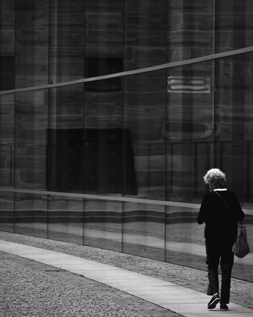 Free Artistic black and white photo of a solitary figure walking alongside reflective glass in Nuremberg, Germany. Stock Photo