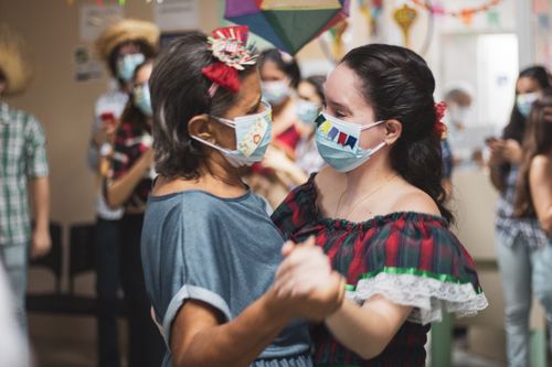 Free Two people in traditional attire dance joyfully with safety masks at a festive indoor event. Stock Photo