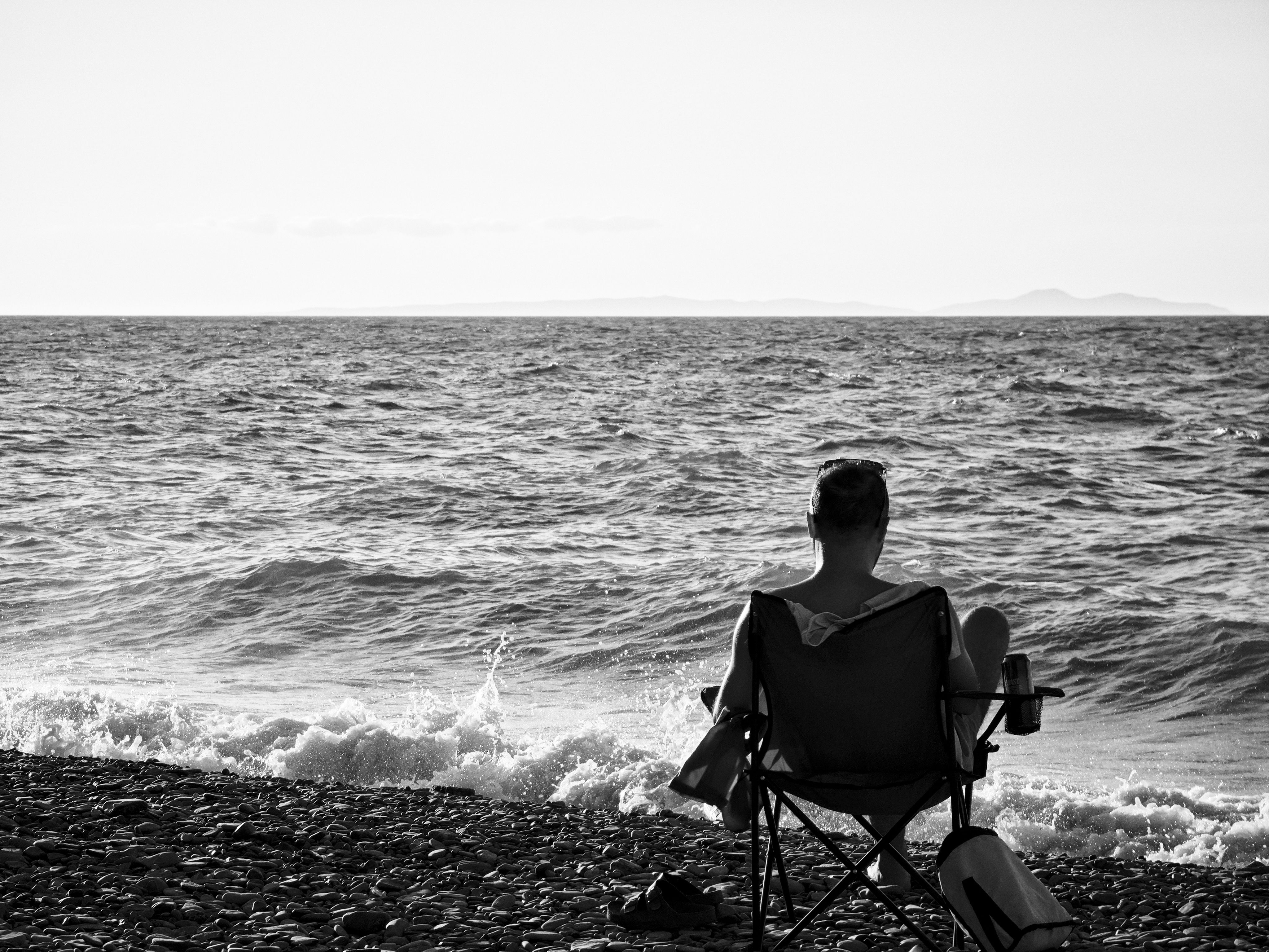 Person sitting alone in a chair by the beach looking out at the ocean — representing the reflective integration period after a bufo retreat