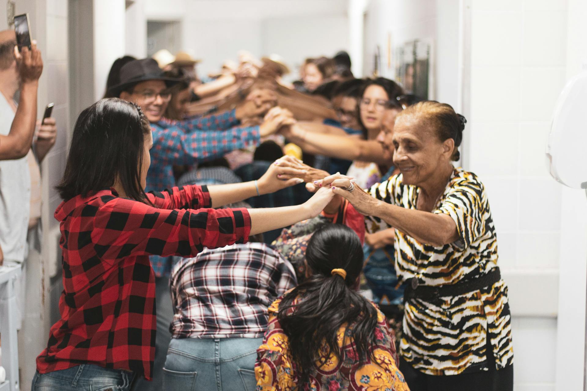 A diverse group of people joyfully holding hands and dancing indoors, symbolizing unity.