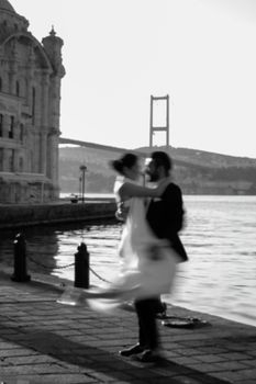 A romantic embrace by a couple near Istanbul's iconic Bosphorus bridge during the day.