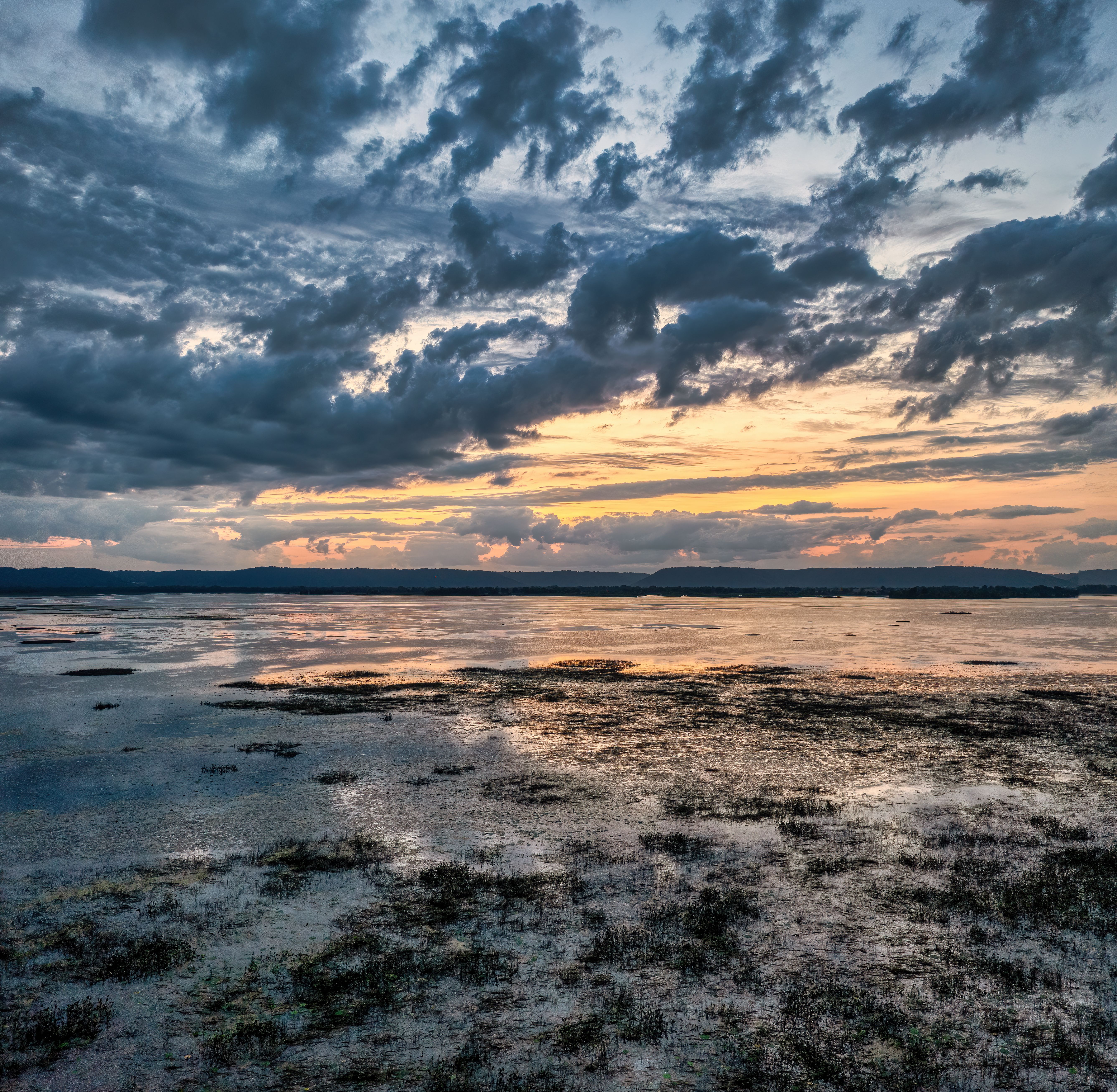 A sunset over a lake with clouds and grass · Free Stock Photo