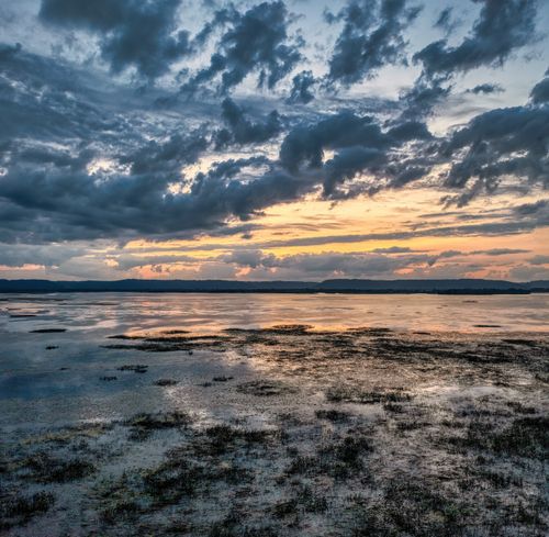 Free Stunning sunset over a tranquil coastal landscape with reflective water and dramatic clouds. Stock Photo