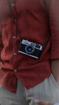 A man in a casual red shirt wearing a vintage camera, showcasing style and leisure indoors.