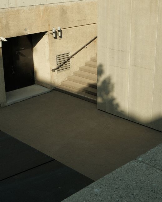 Minimalist urban architecture featuring concrete steps, shadows, and a black door in soft daylight.