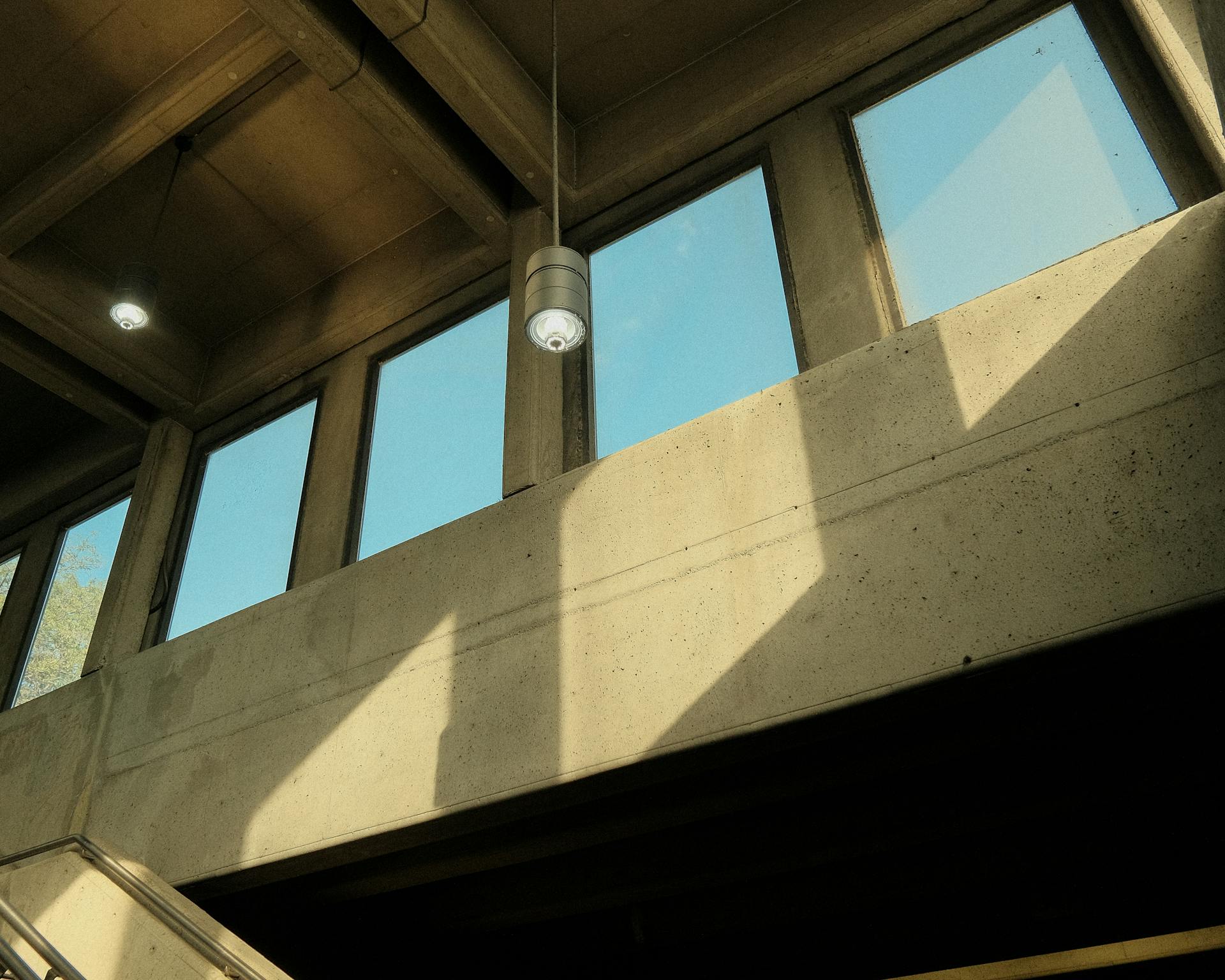 Concrete interior with large windows and natural light casting shadows indoors.