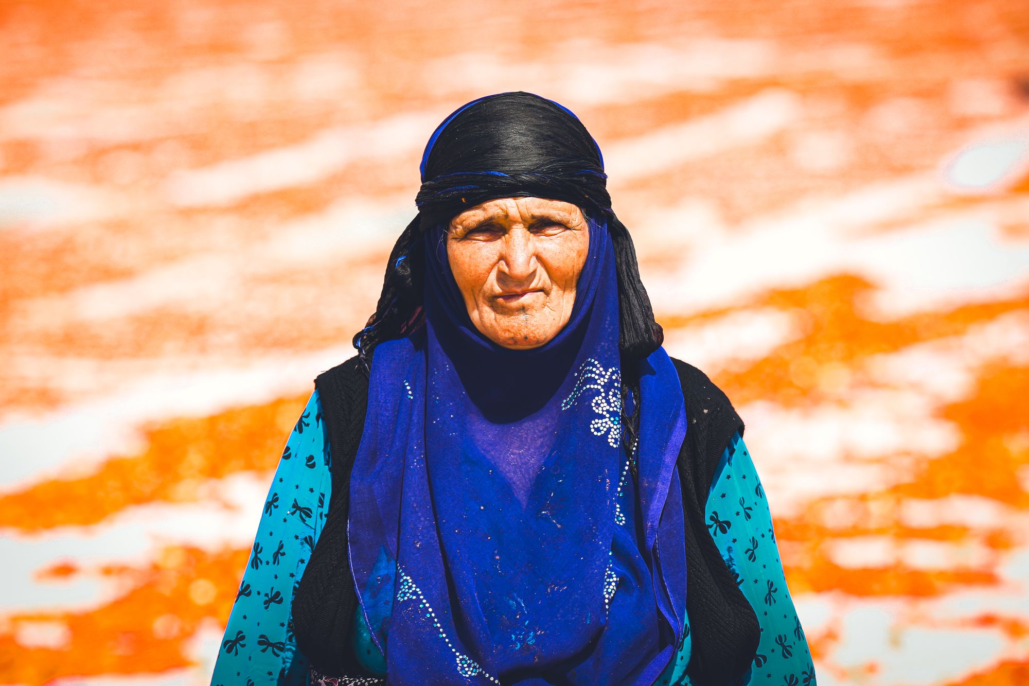 Portrait of an elderly woman with a blue veil in a sunny outdoor setting.