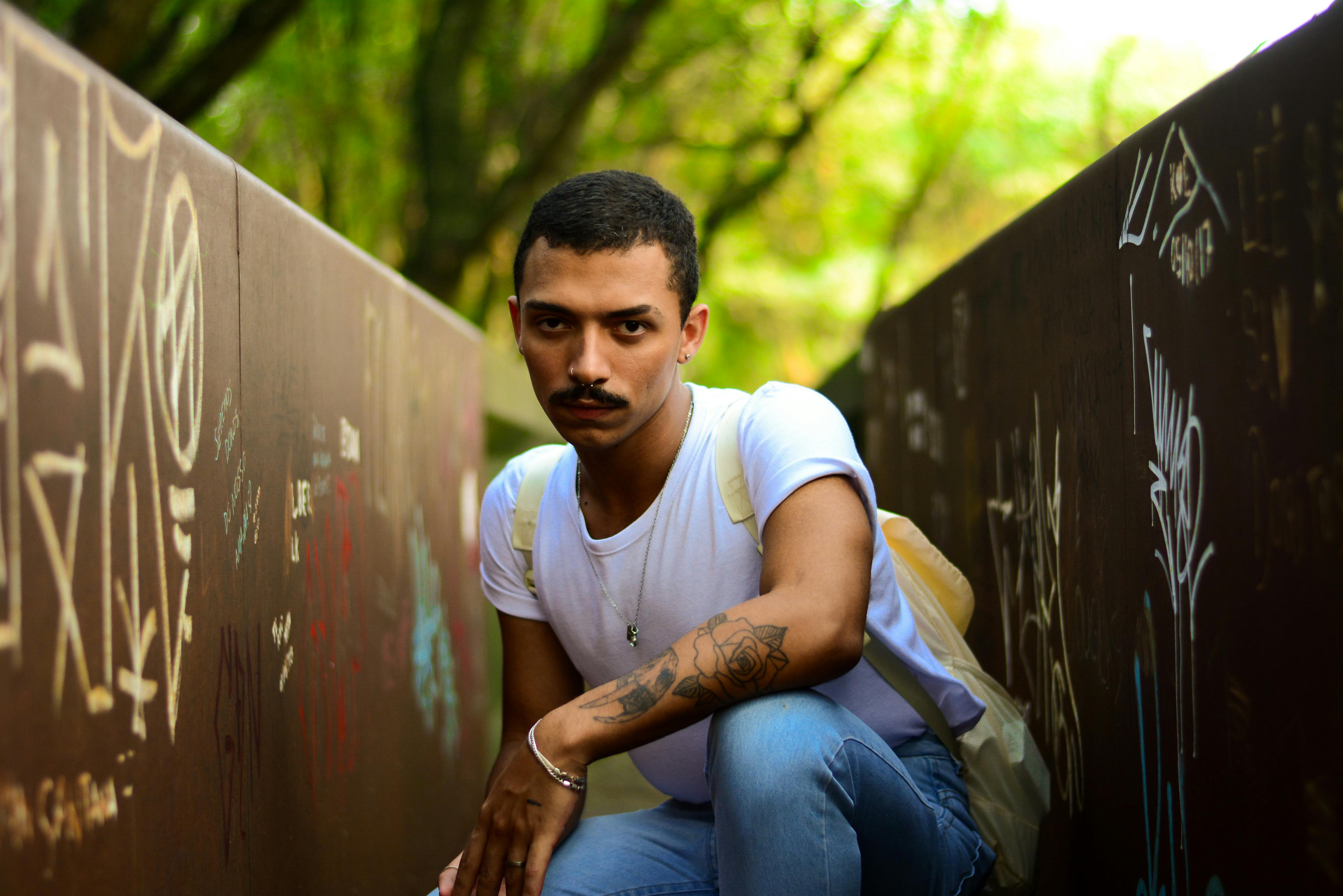 a man in a white shirt and jeans crouches down on a wall