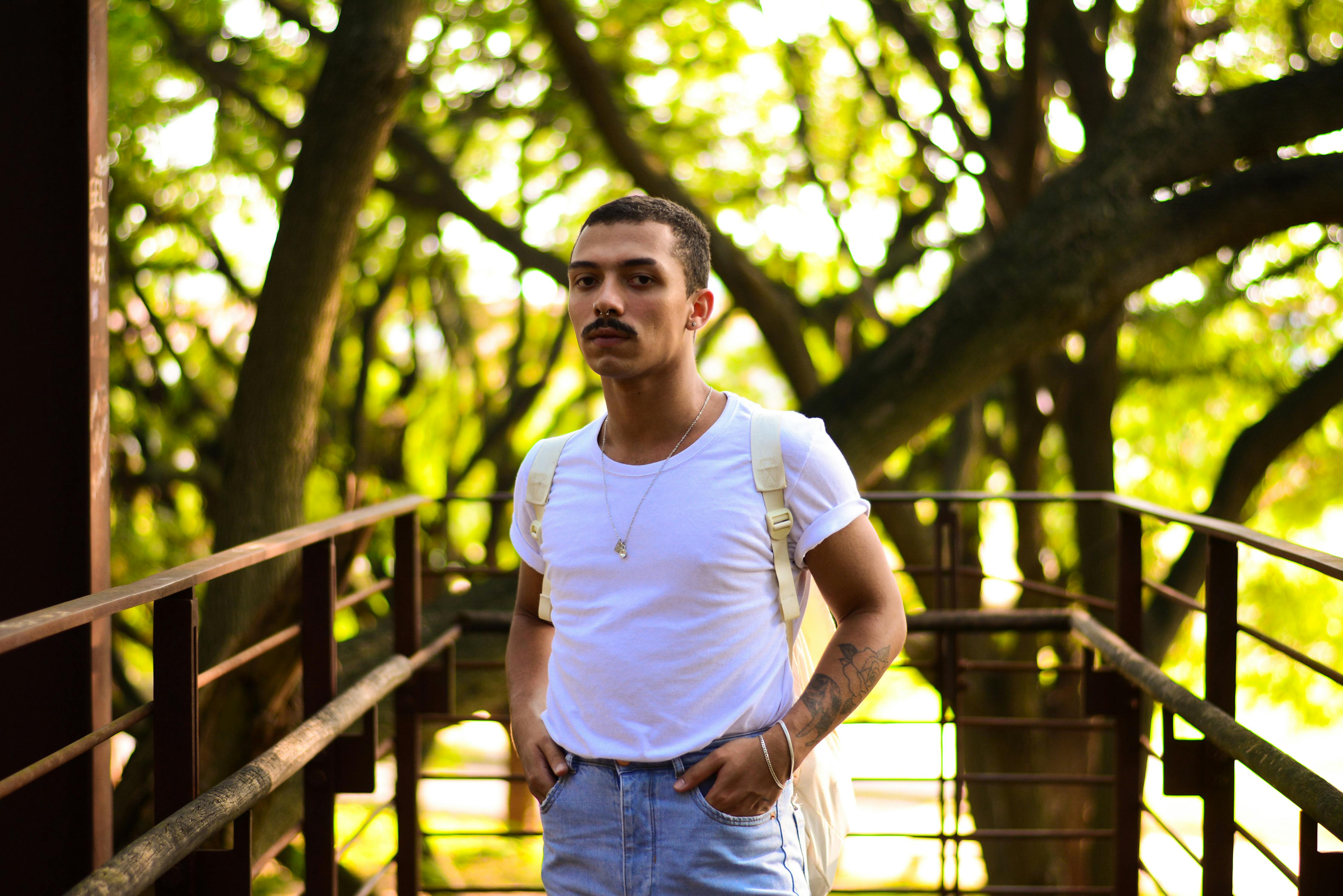 a man in a white t shirt and jeans standing on a bridge