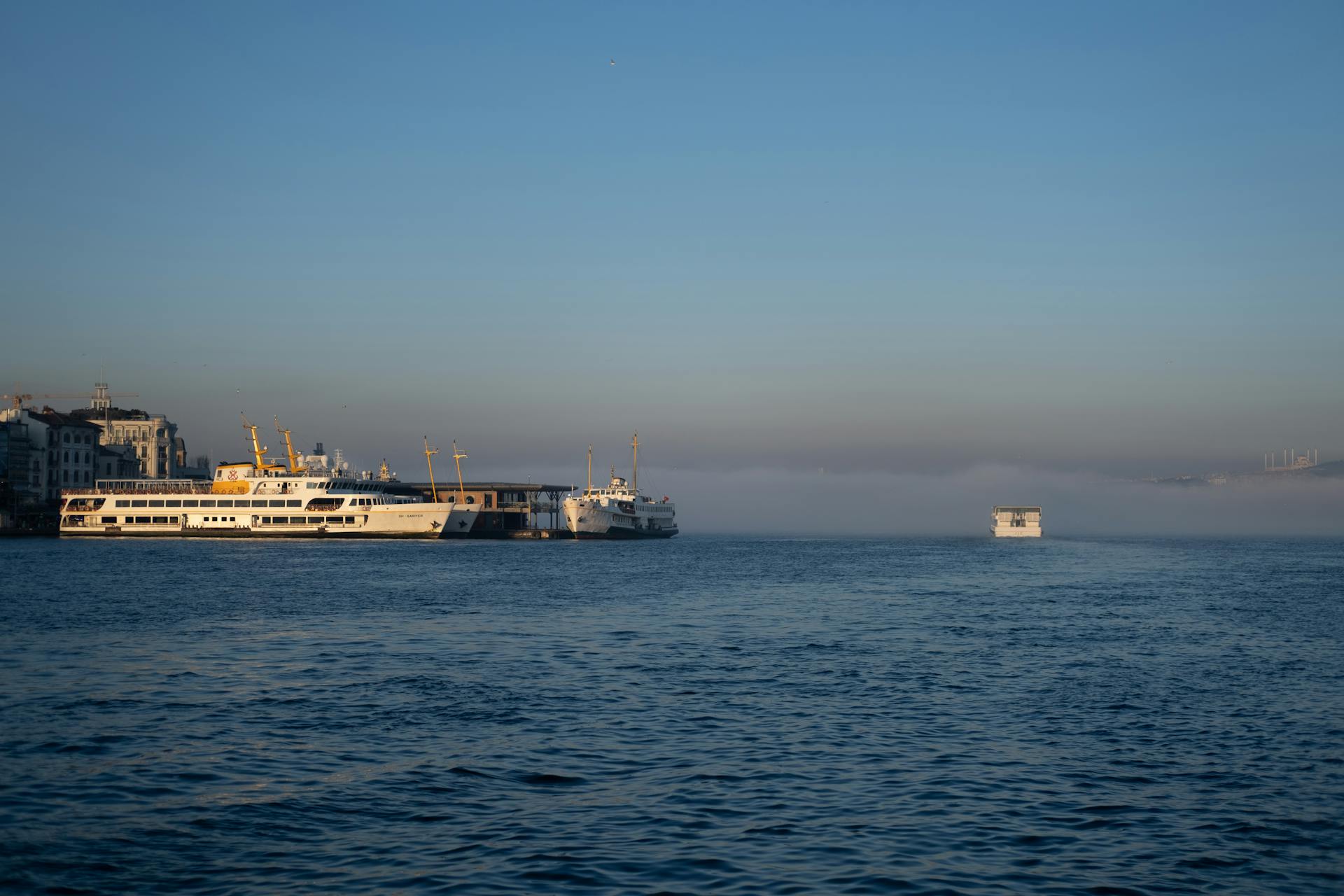 Passenger ferries docked at a serene harbor with misty waters under a clear sky.