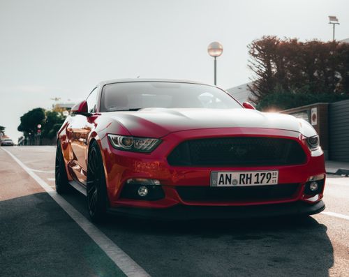 Free A sleek red sports car parked on a sunlit city street, showcasing automotive elegance. Stock Photo