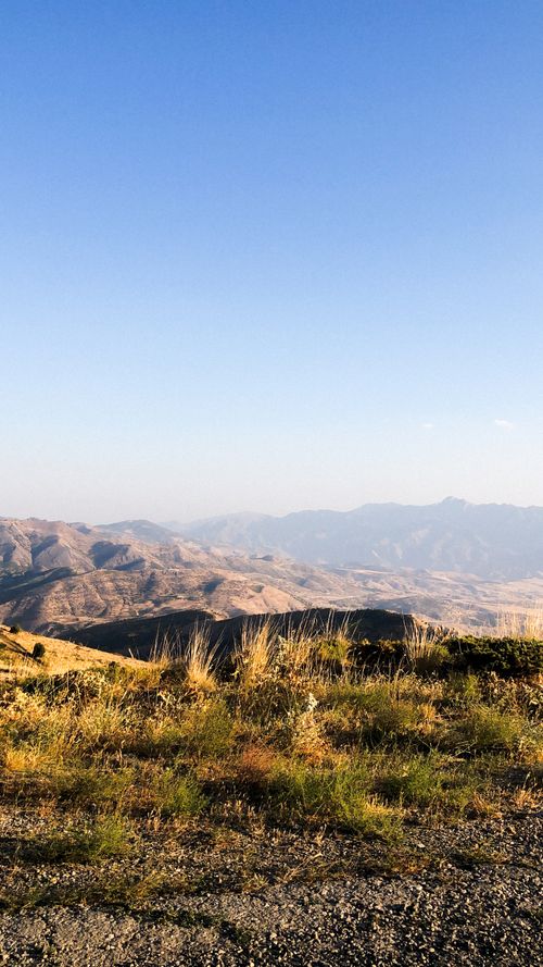 Free Scenic view of a sunlit arid mountain landscape with dry grass under a clear blue sky. Stock Photo