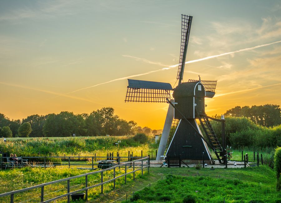 A serene sunset over a traditional windmill in a rural Netherlands landscape.