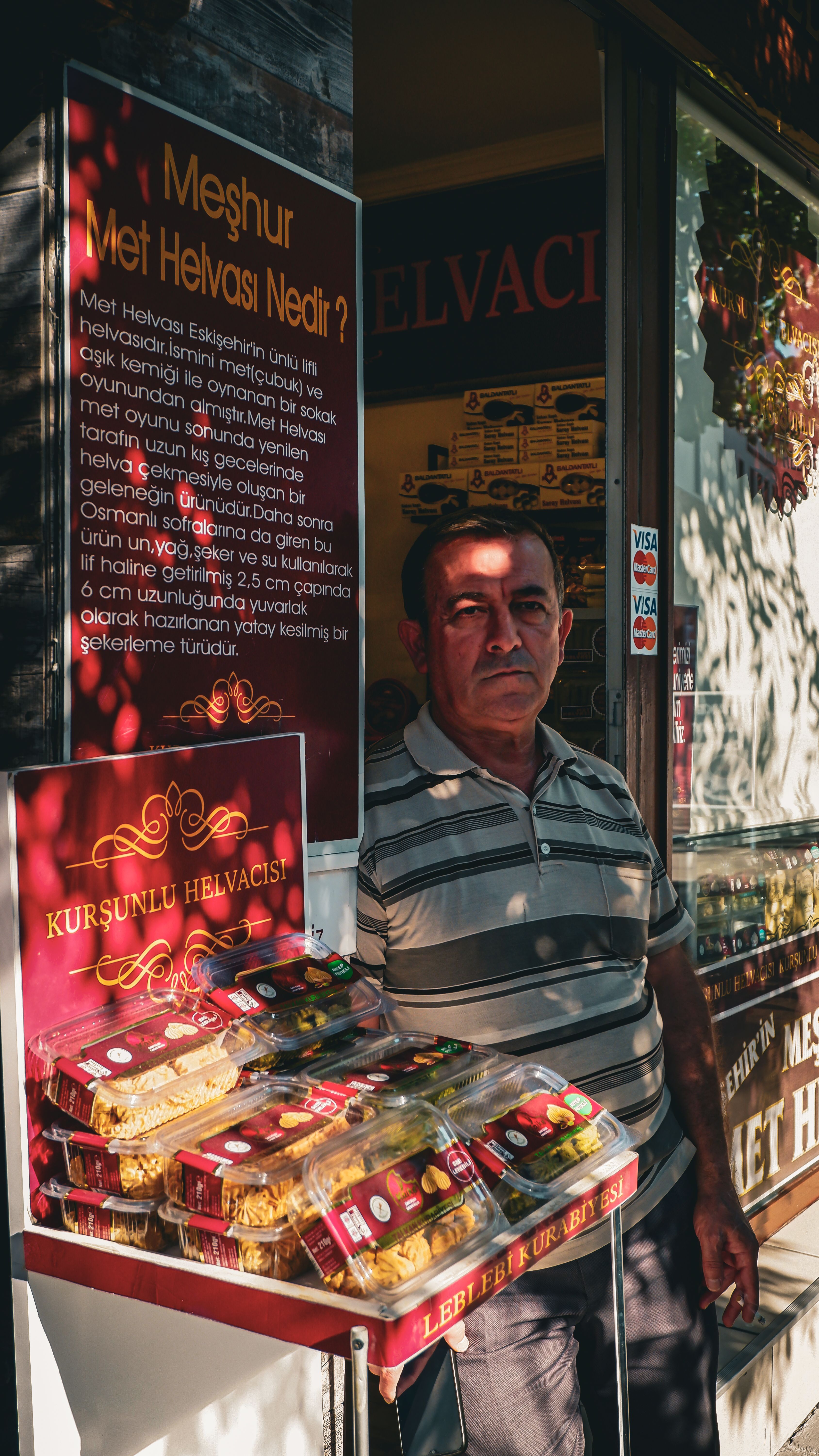 A man stands beside a display of traditional Turkish desserts outside a shop in Eskişehir.
