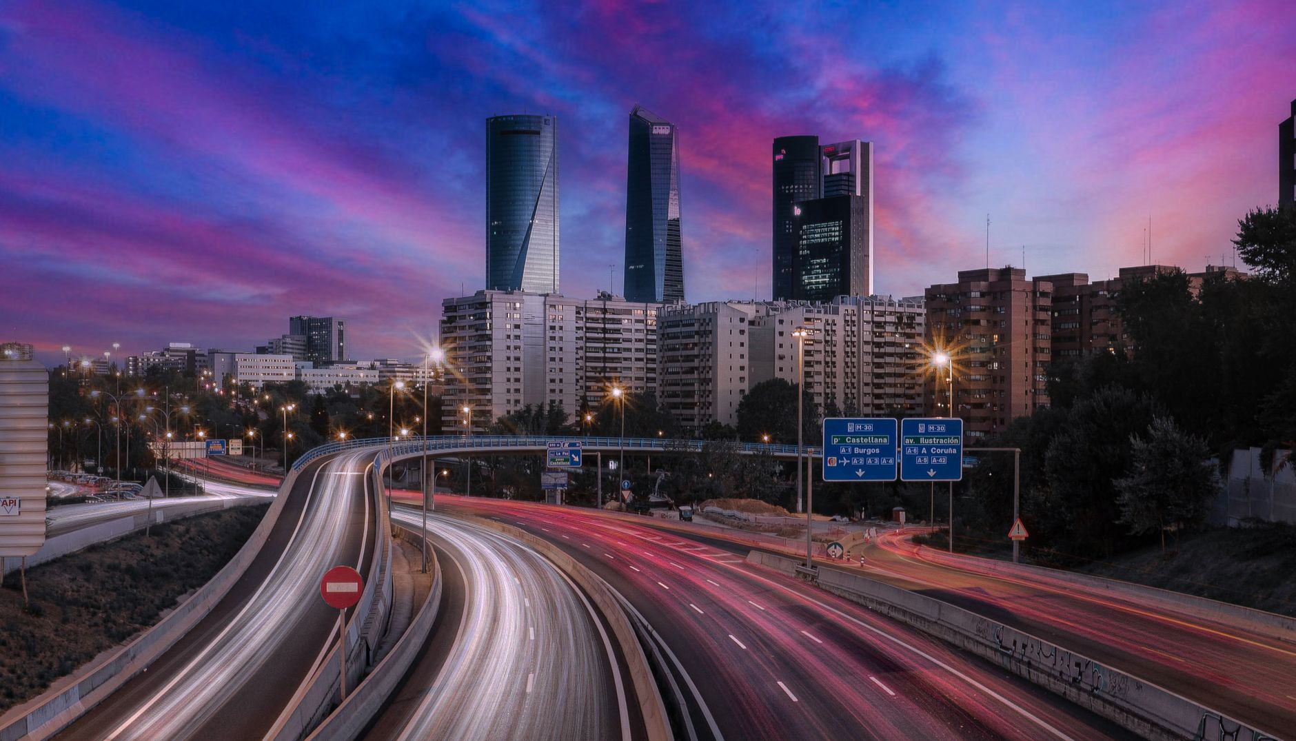 Captivating view of Madrid's skyline and highway during twilight featuring striking light trails.