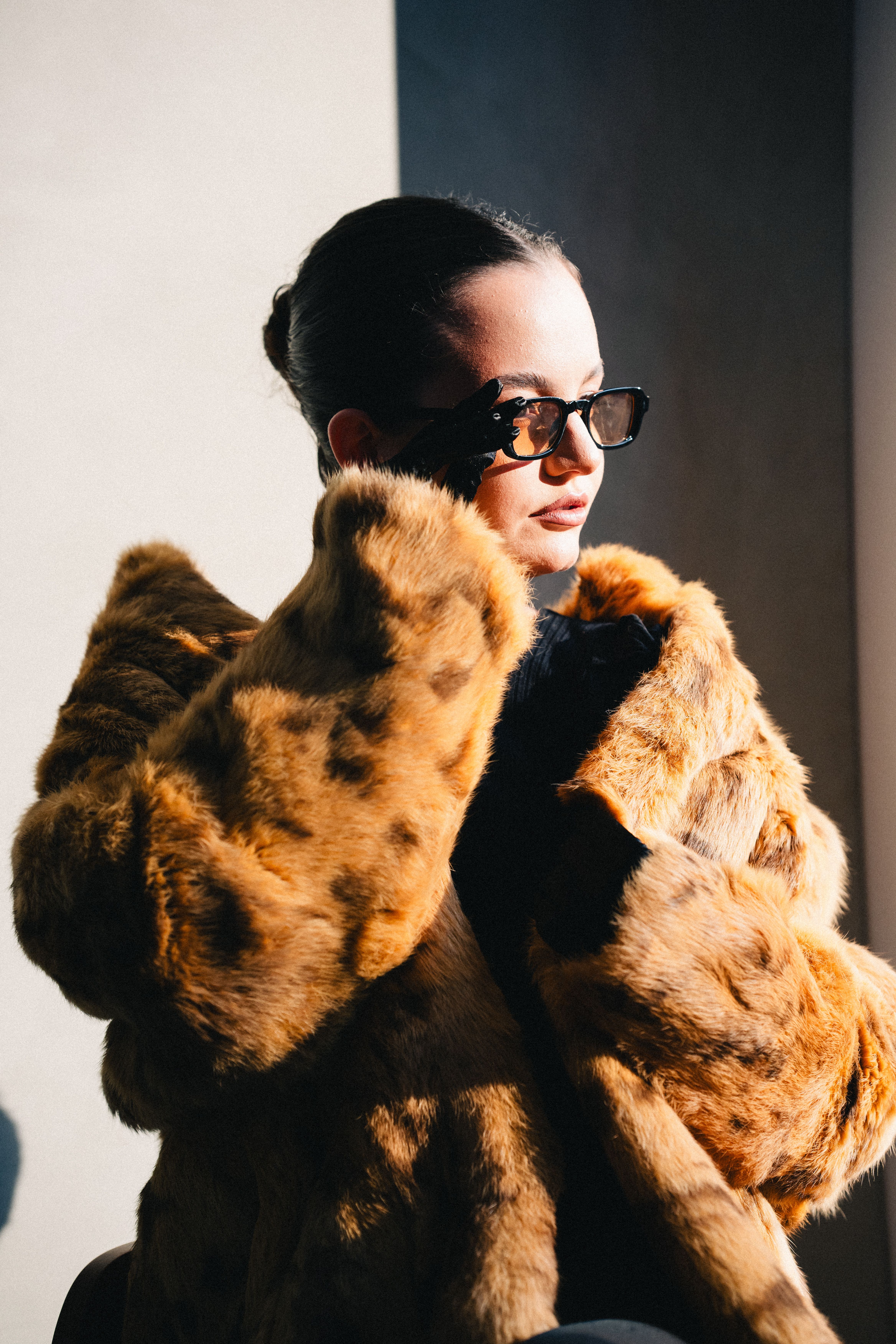 Elegant woman in a fur coat basking in sunlight, exuding luxury and style.