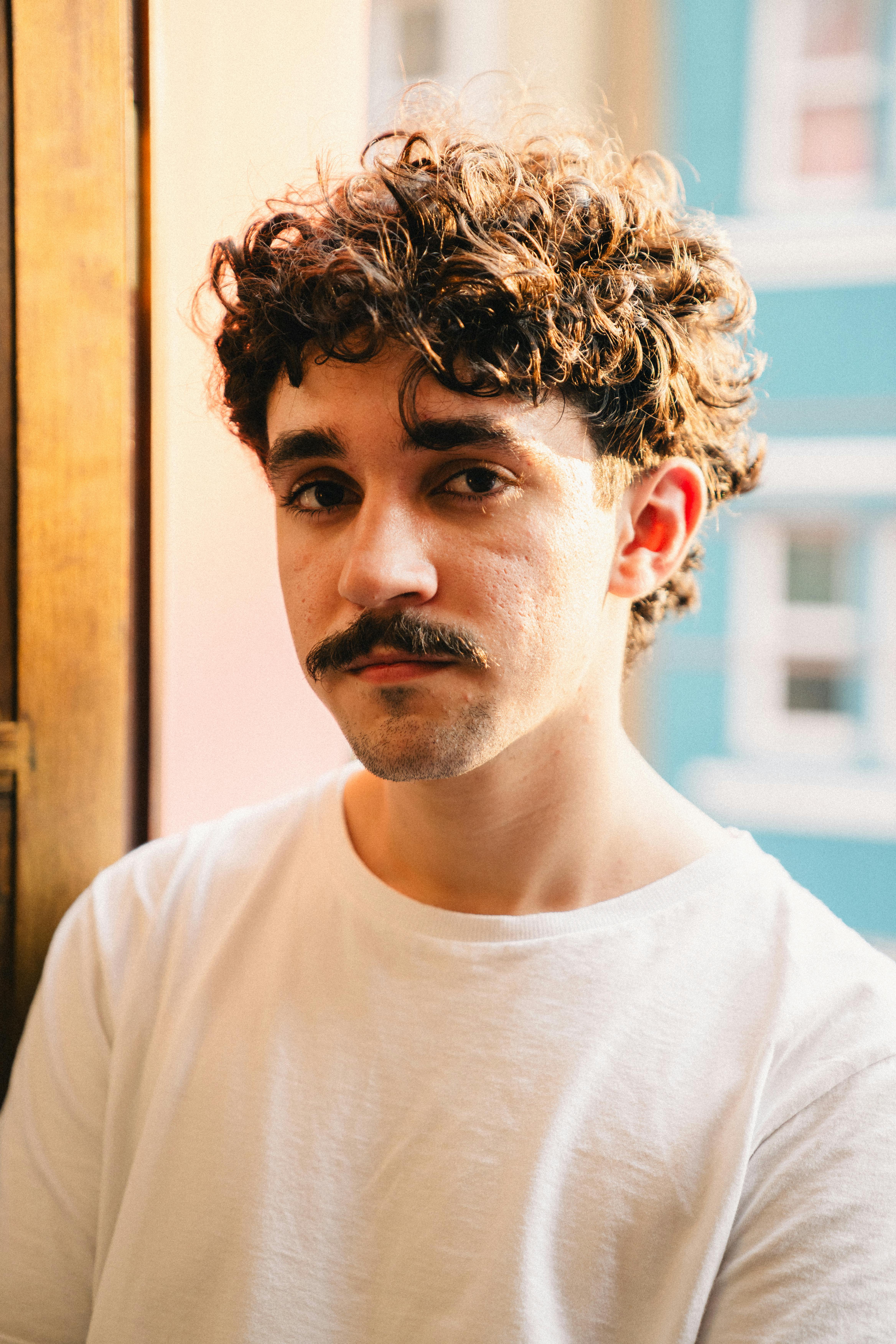 portrait of young man in white shirt with mustache and curly hair