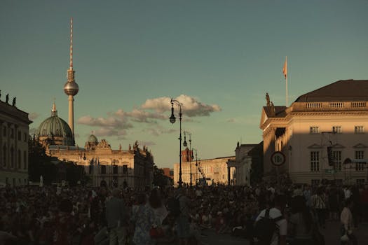 Large crowd enjoys a vibrant sunset near Berlin's TV Tower and historic architecture.