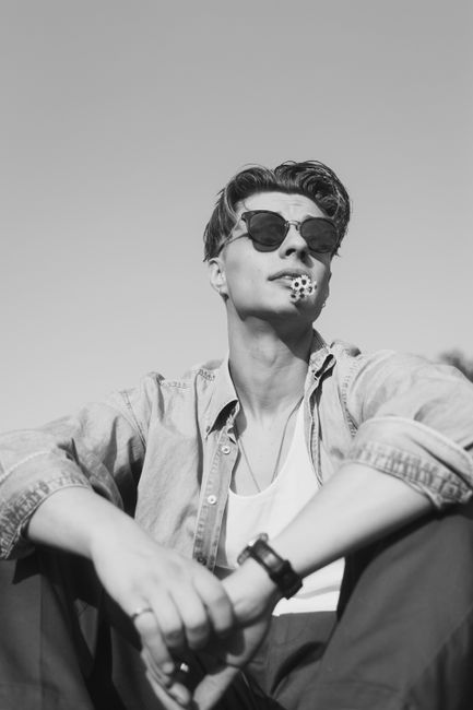 Fashionable man with sunglasses holding a flower in mouth, black and white portrait.