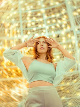 Fashionable woman posing artistically with golden lights in the background.