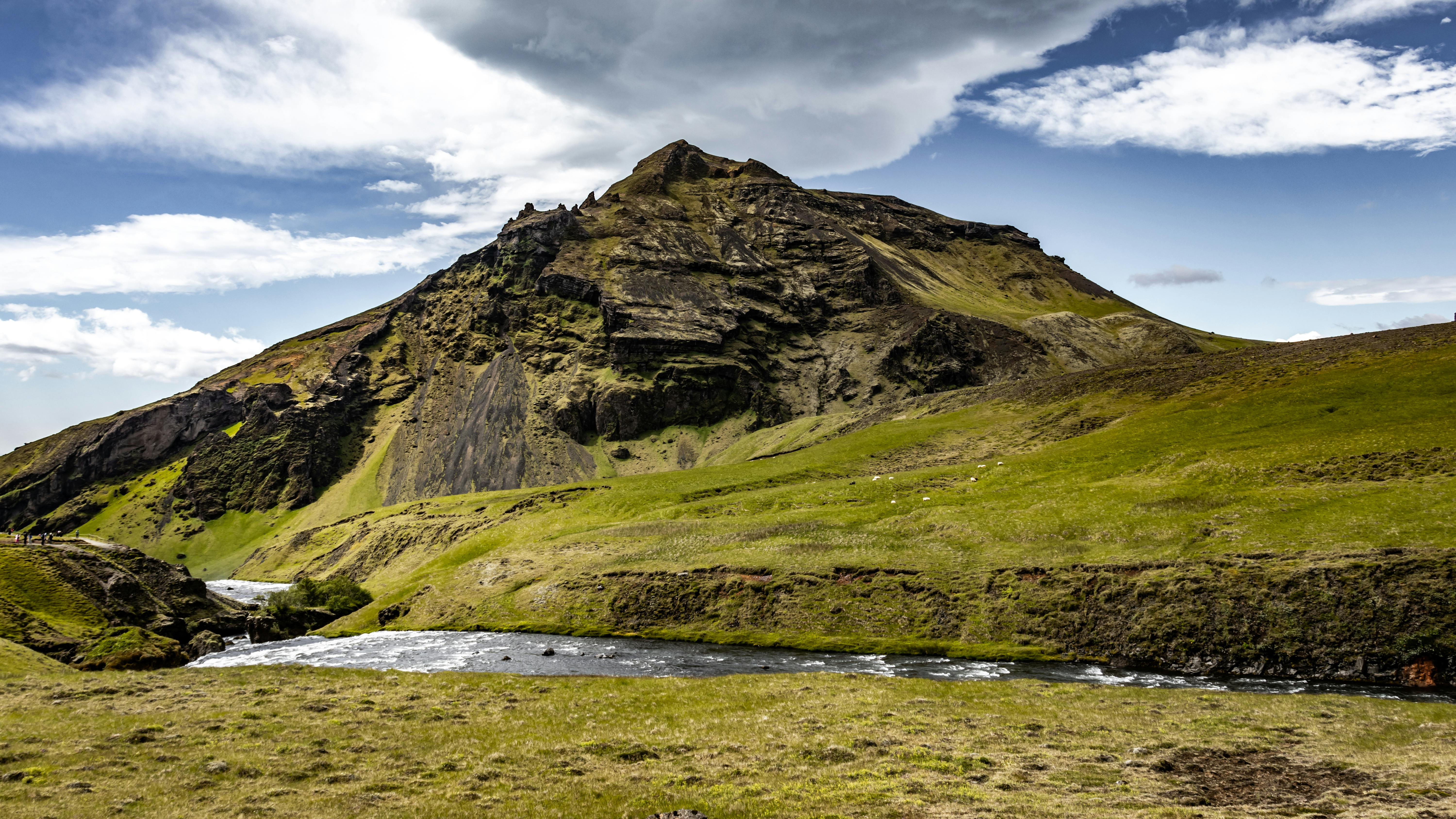 Picturesque mountain landscape in Iceland with lush green hills and flowing river under a dramatic sky.