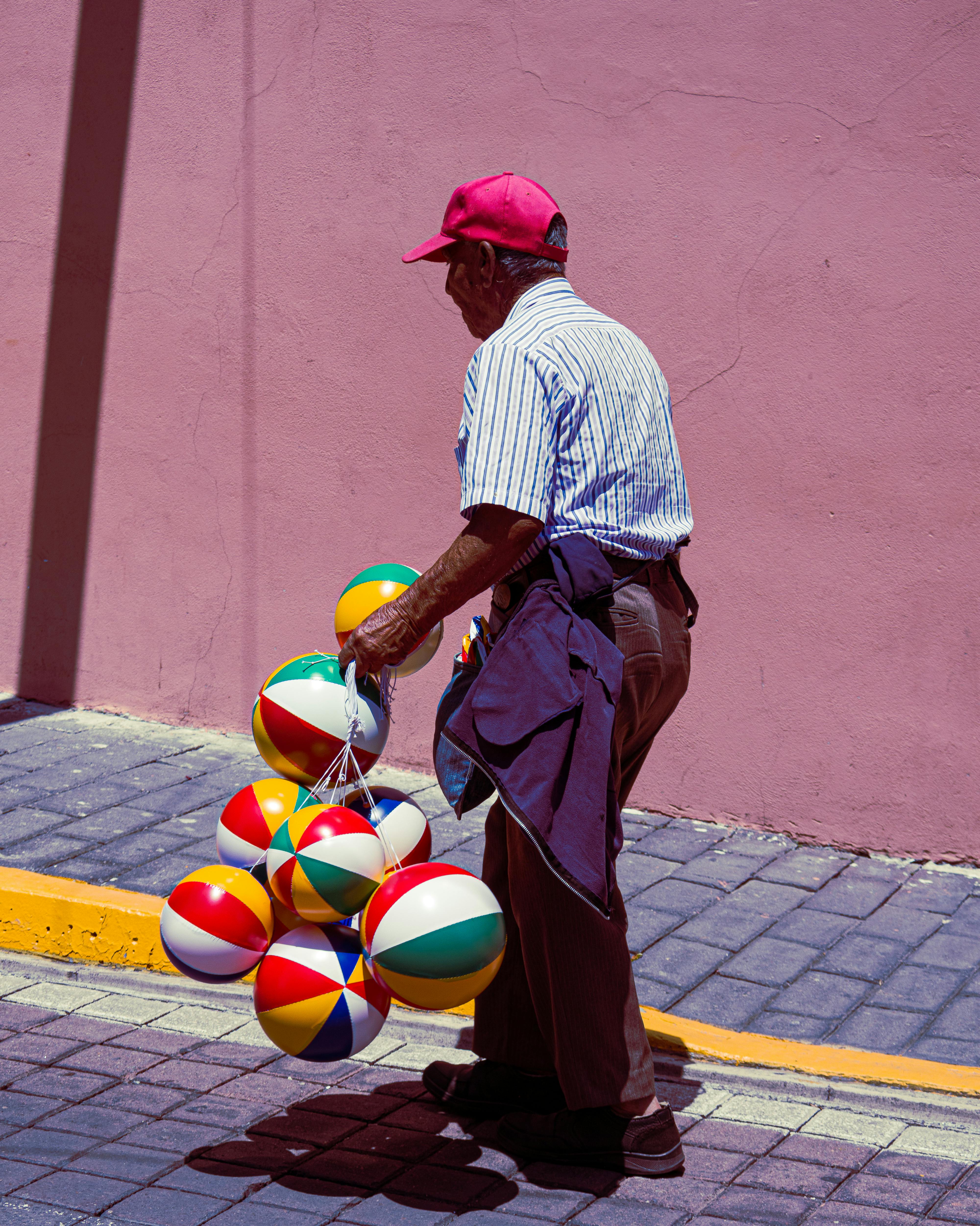 A man in a vibrant street scene sells colorful beach balls, creating a lively urban atmosphere.
