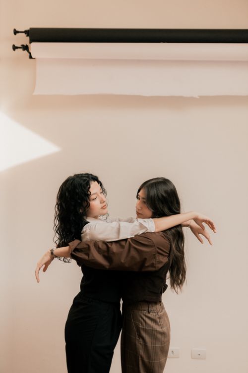 Free Two women sharing a warm hug in a studio with soft lighting and a neutral background. Stock Photo