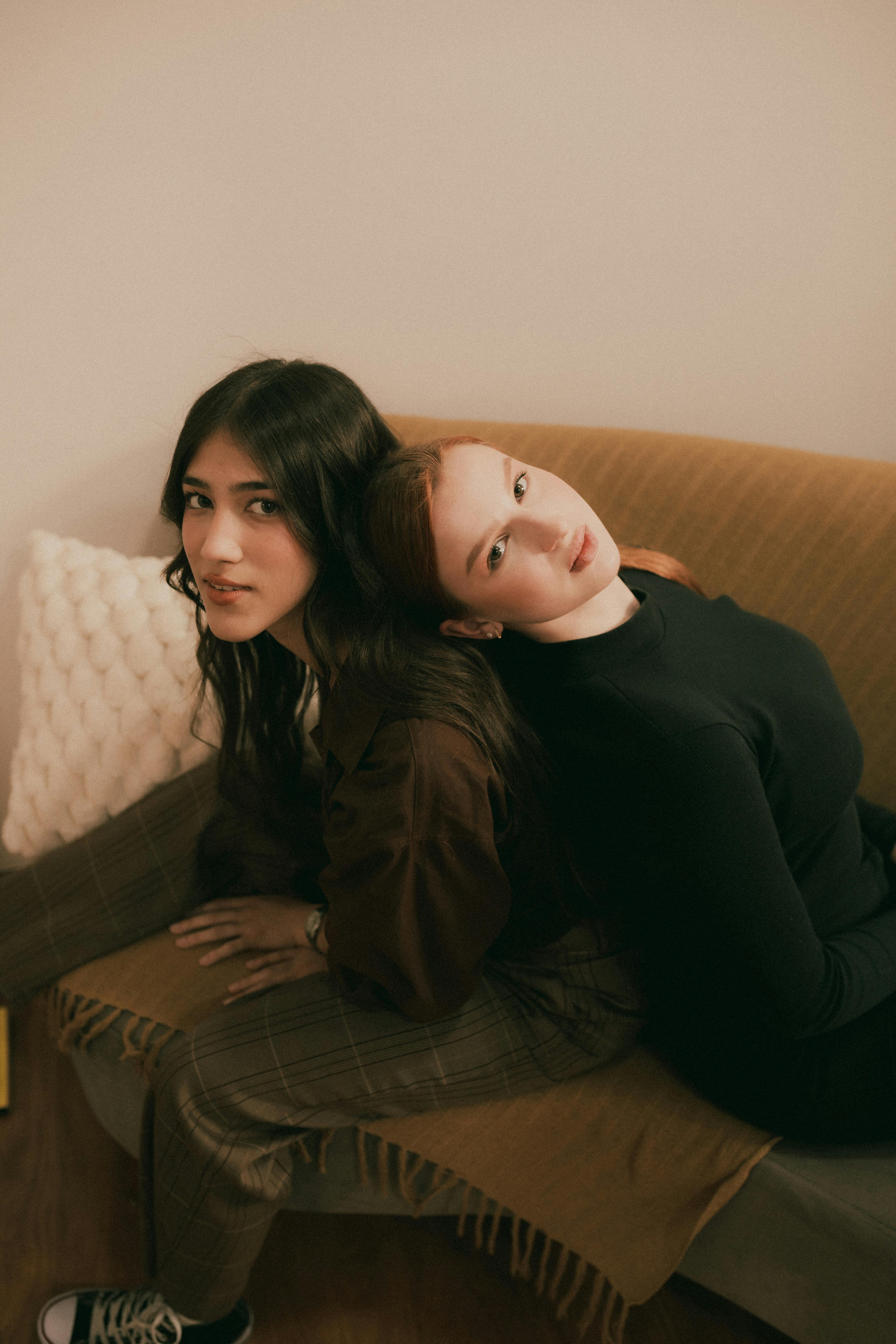 Two women seated comfortably indoors, sharing a relaxed moment on a sofa.
