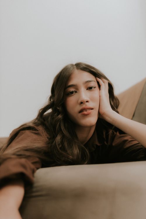 Free A young woman with long hair relaxes comfortably on a couch indoors, conveying tranquility. Stock Photo