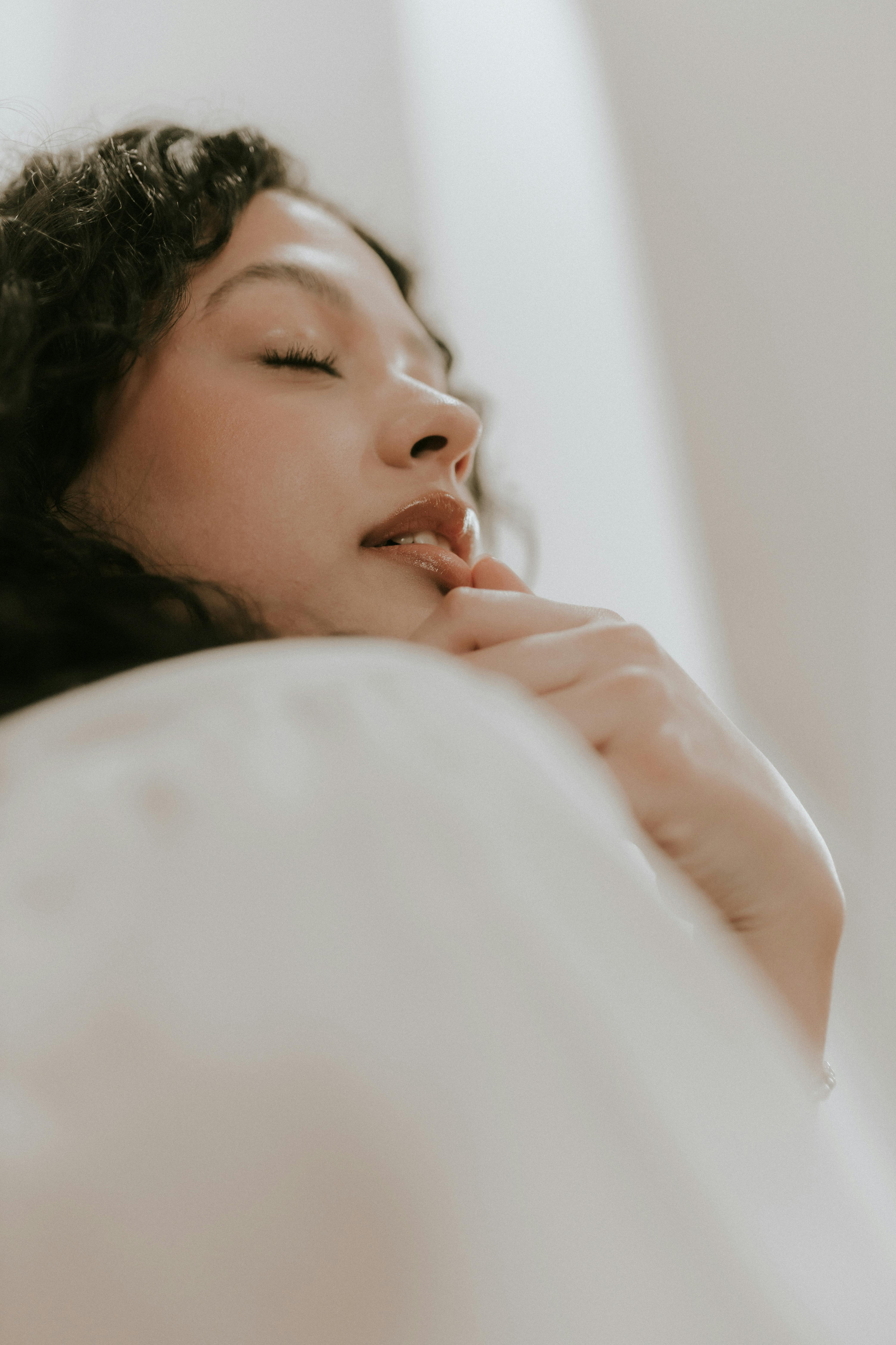 Close-up portrait of a relaxed woman with closed eyes indoors, captured in soft natural lighting.