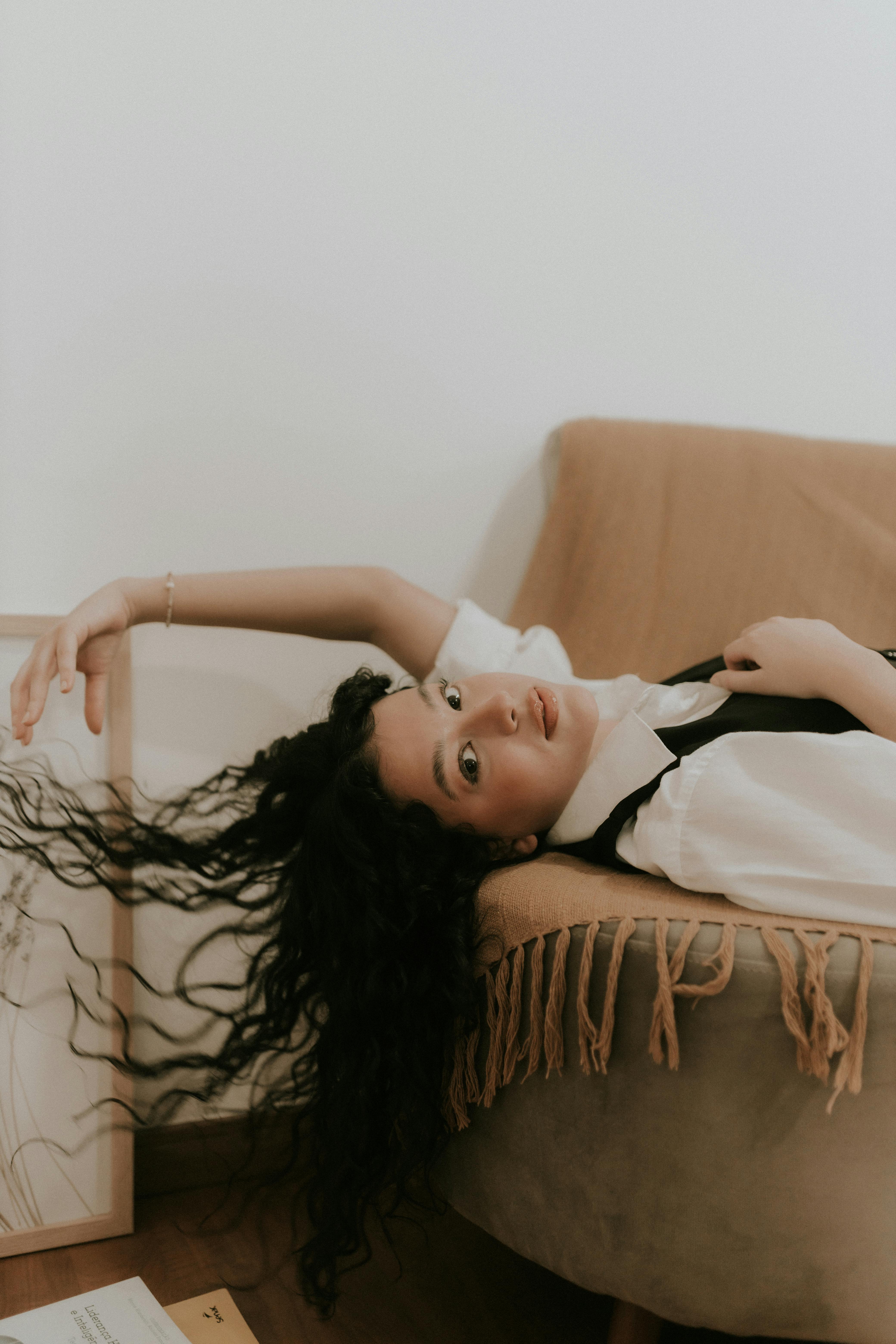 Young woman with curly hair reclining elegantly on a sofa indoors, creating a serene and relaxed mood.