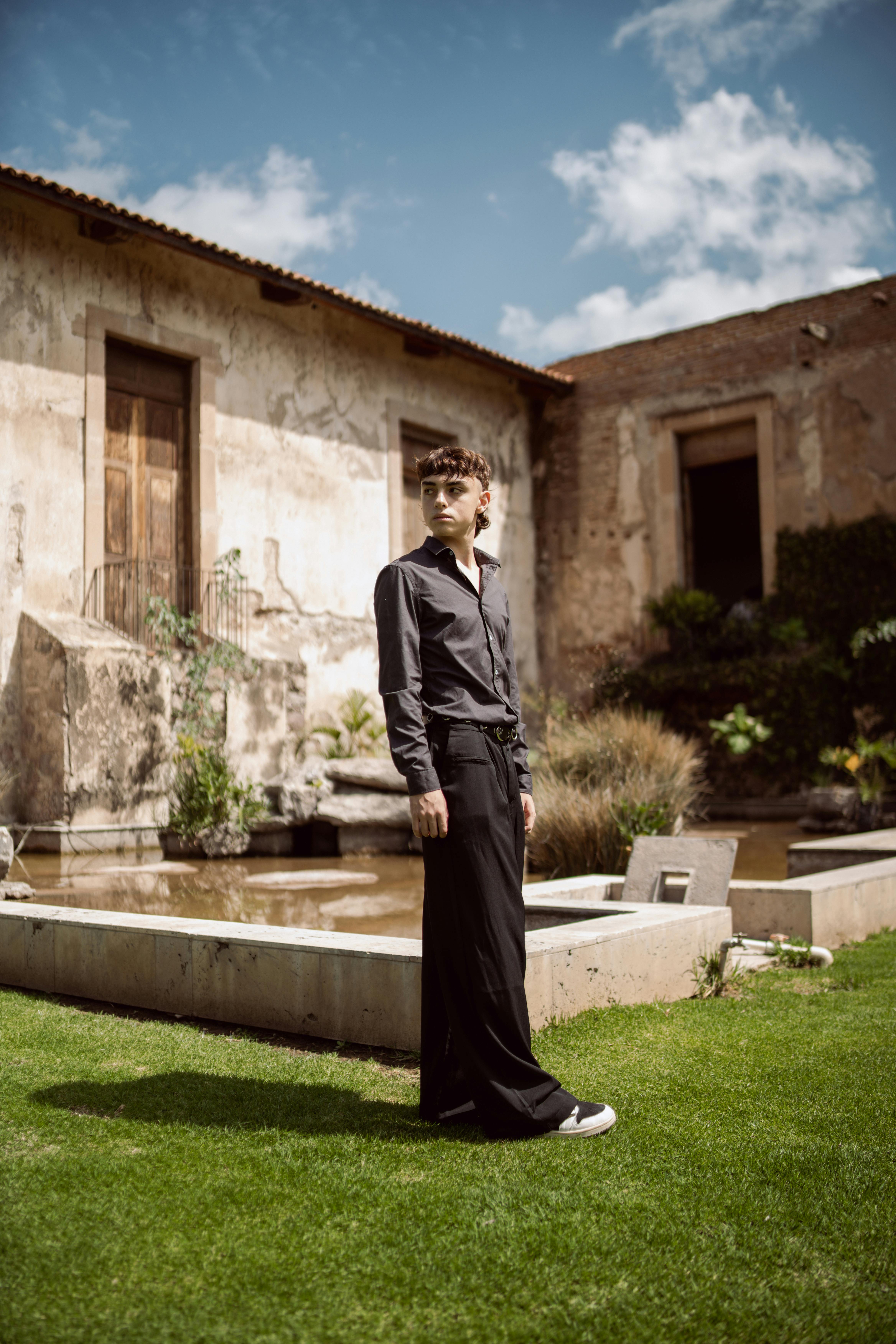 Stylish man in a black outfit standing in a rustic garden, showcasing modern fashion.