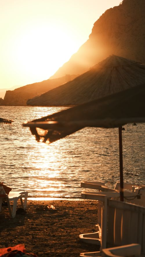 Free A serene beach at sunset with umbrellas and chairs, perfect for vacation vibes. Stock Photo