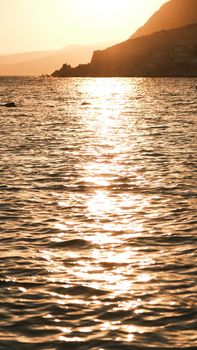 Beautiful golden sunset reflecting on ocean waves with a silhouette of a coastline.