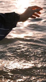 A serene image of a hand gently touching a shimmering water surface at sunset.