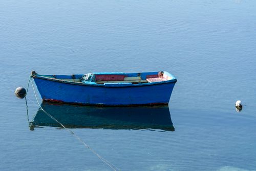 Free A blue boat floats peacefully on clear water with a gentle reflection. Stock Photo