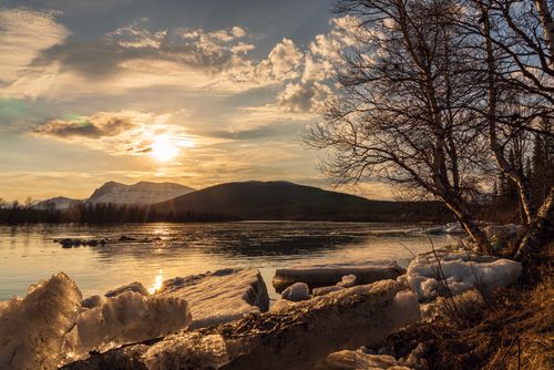 Free Beautiful winter sunset with ice formations on a serene lake surrounded by mountains. Stock Photo