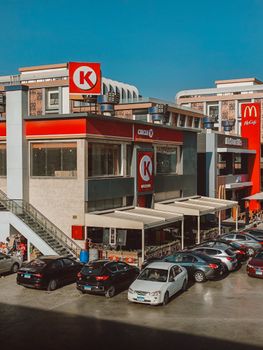 Busy shopping center with fast food chains and parking lot, sunny day.