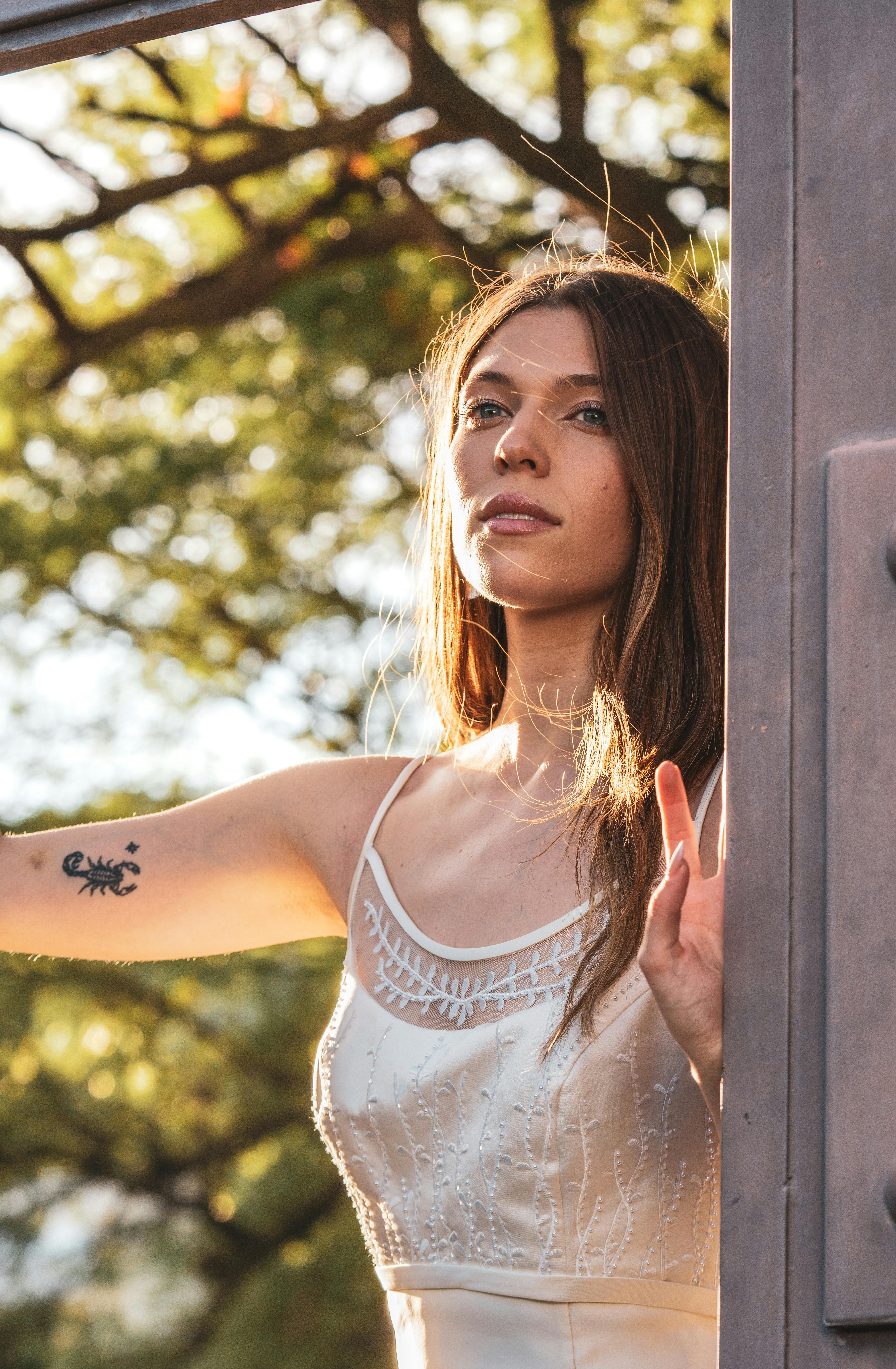 A beautiful woman in a white dress enjoys the warm sunlight in a garden setting.