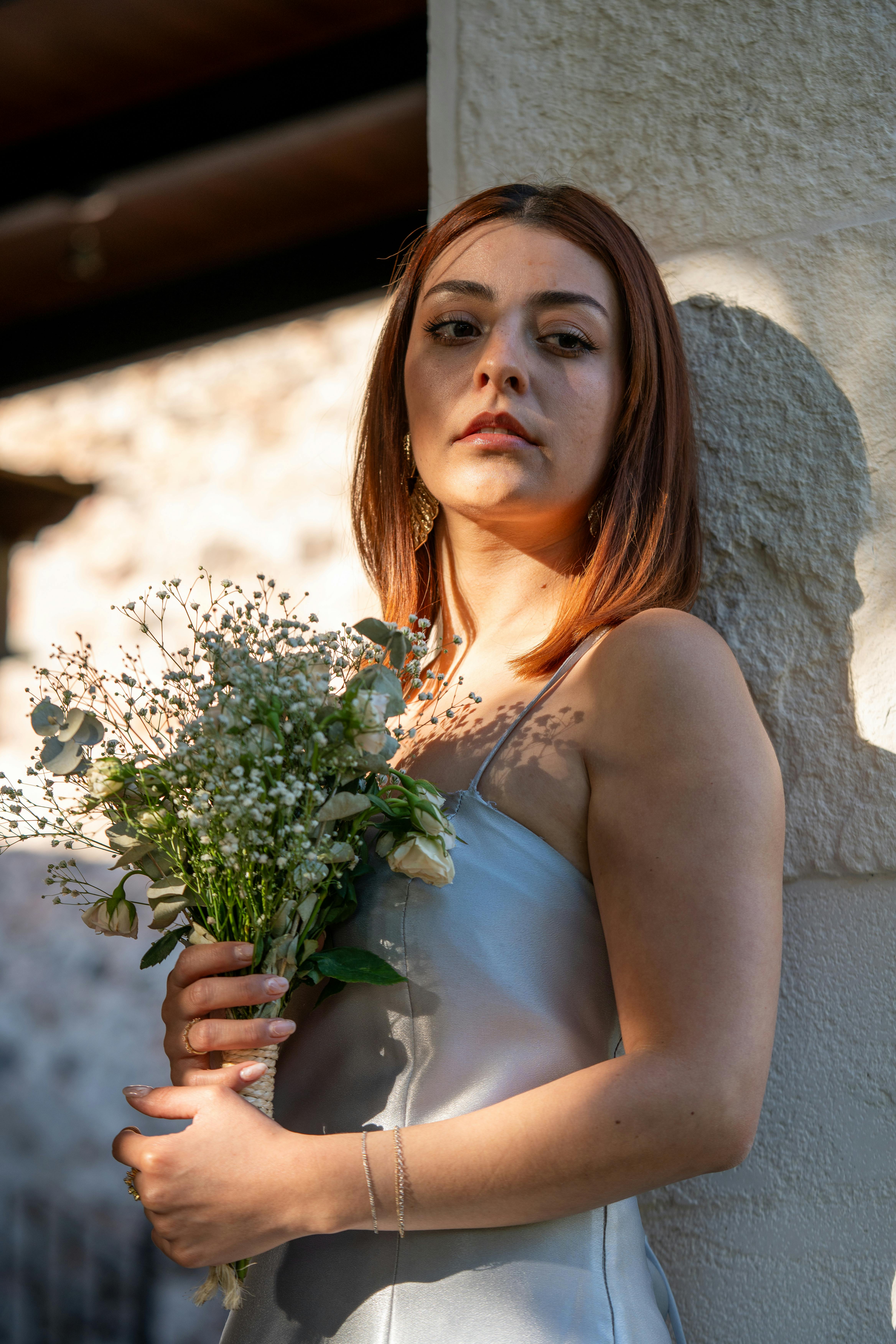Elegant portrait of a bride holding a bouquet in a summer setting, showcasing minimalist bridal fashion.