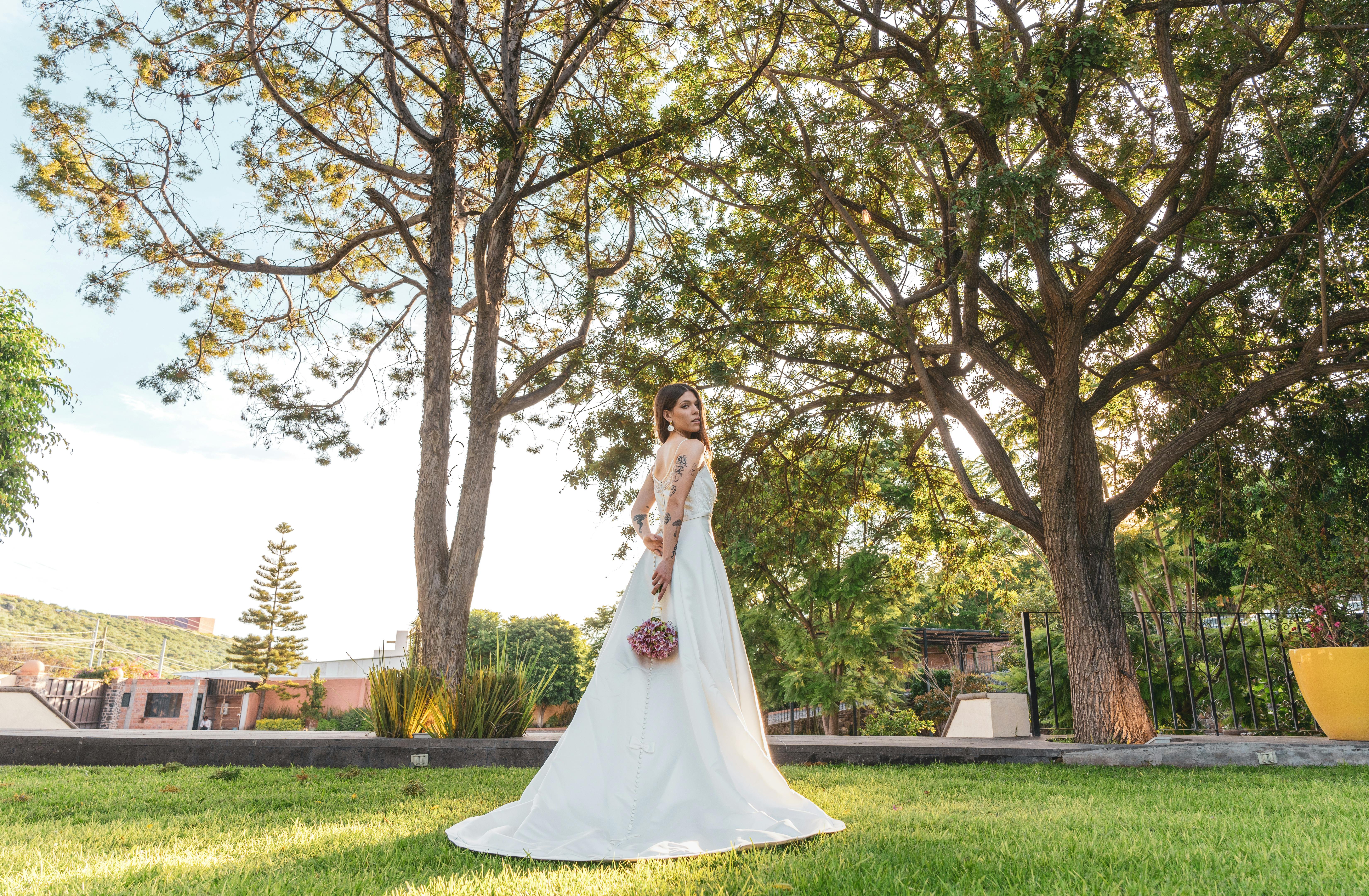 Beautiful bride in a sunlit garden with lush greenery, holding a bouquet.