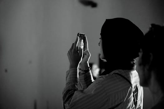 Silhouette of a woman in profile taking a photo with her phone indoors.