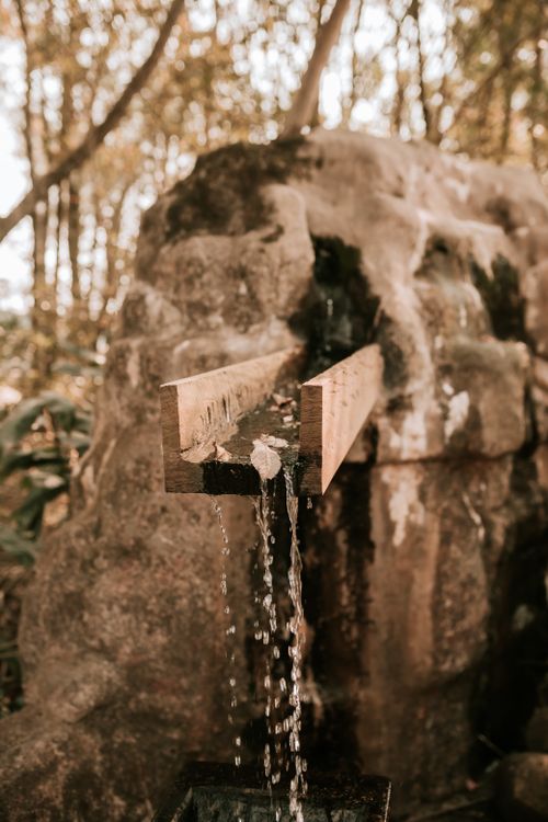 Free Serene scene of water flowing from a wooden spout set in a rocky landscape. Stock Photo