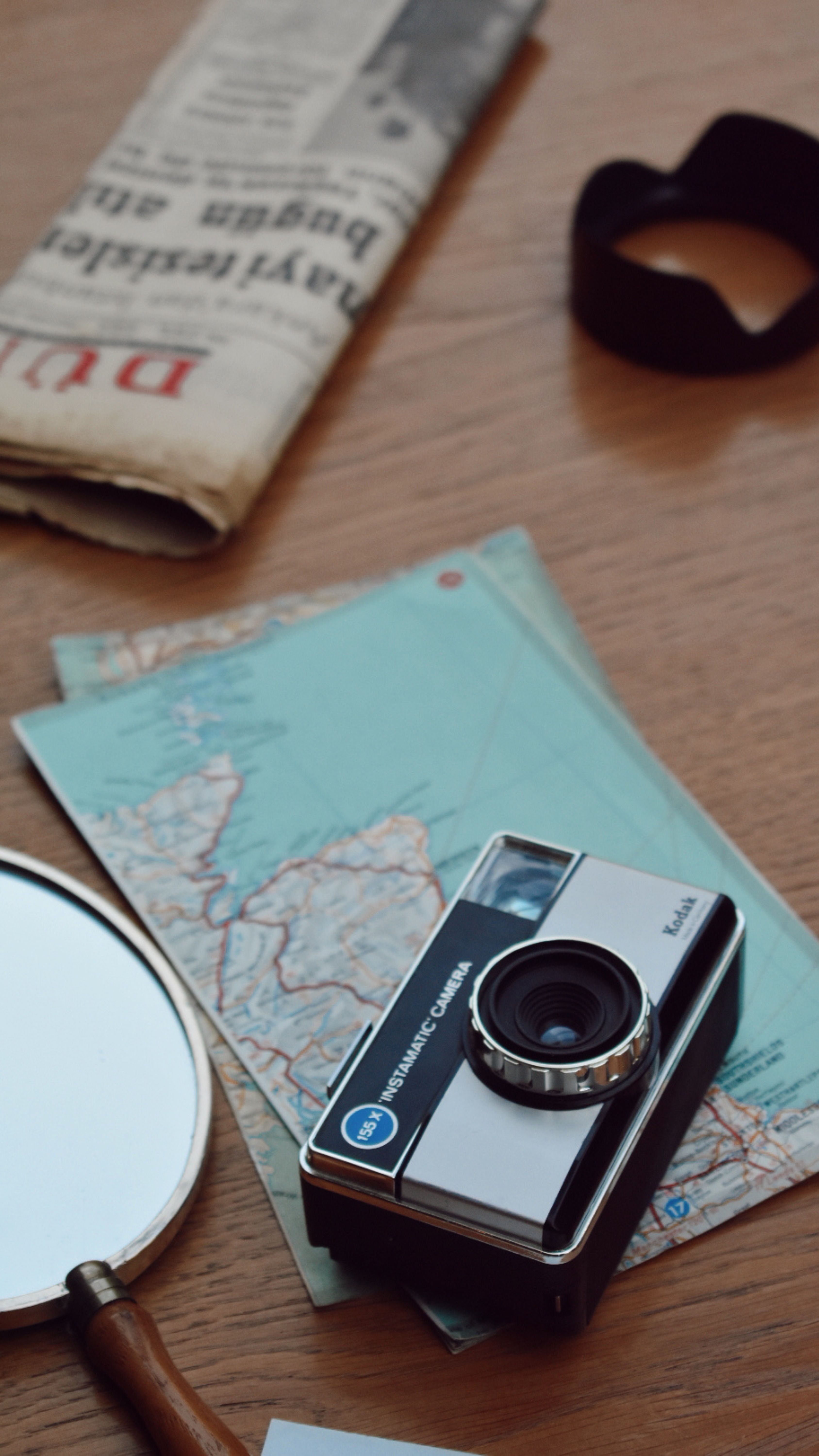 A vintage camera, maps, and newspaper on a wooden table create a nostalgic travel vibe.