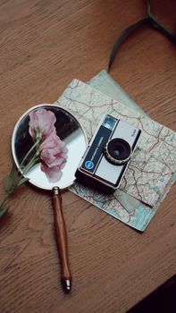 A vintage camera, map, and mirror with flowers on a wooden table, evoking travel nostalgia.