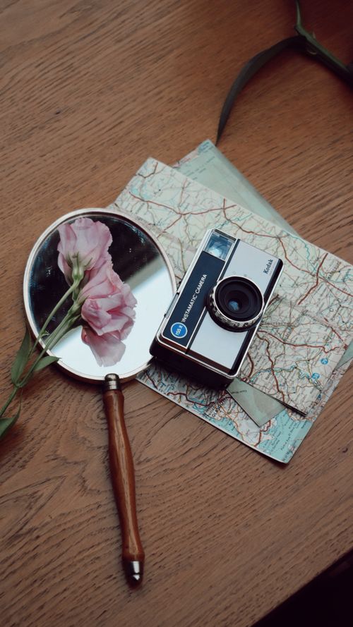 Free A vintage camera, map, and mirror with flowers on a wooden table, evoking travel nostalgia. Stock Photo