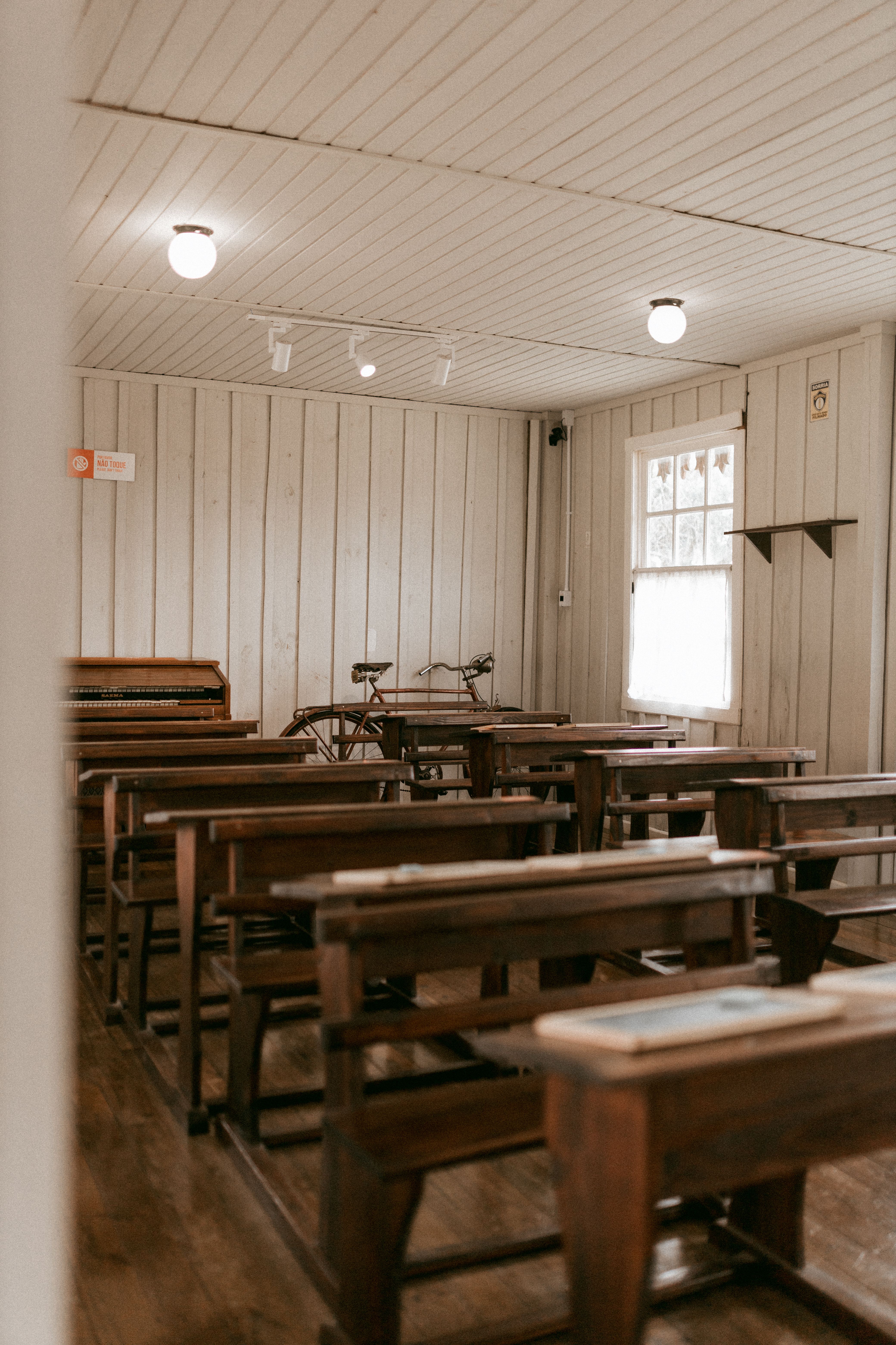Interior of an old wooden classroom with benches, desks, and a vintage piano, conveying a nostalgic educational setting.